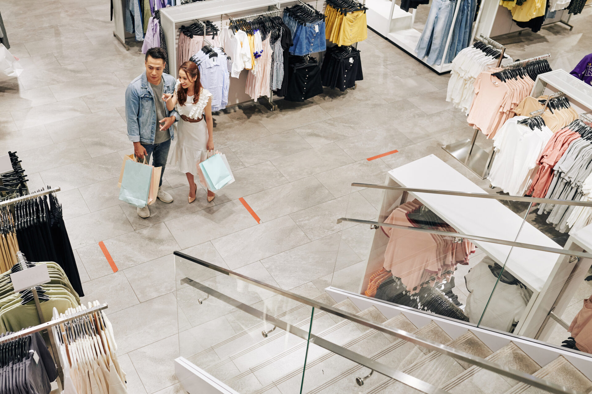 Positive young Vietnamese couple walking in shopping mall and buying clothes and shoes on sale