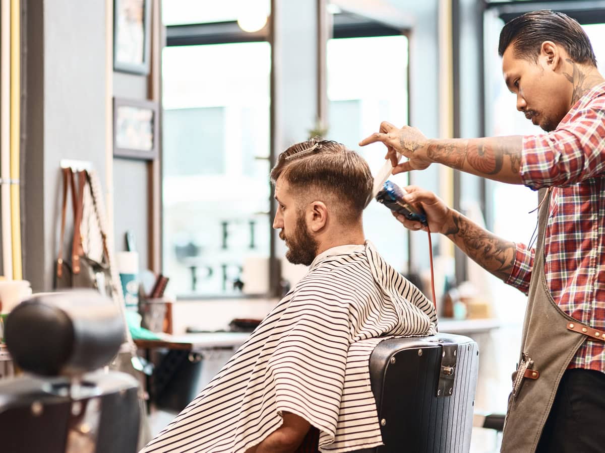 concentrated professional barber makgng a haircut for a bearded man
