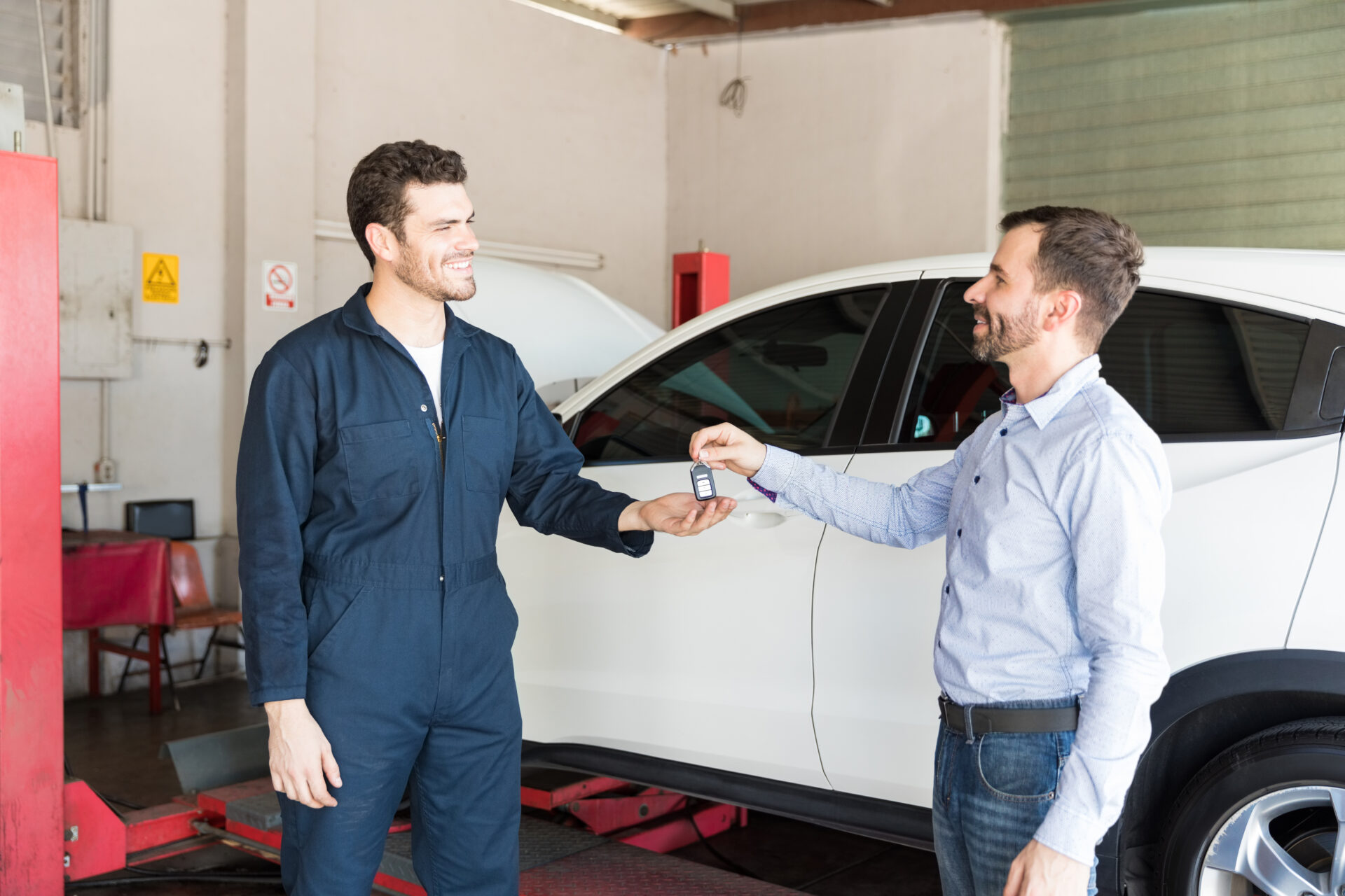 customer handing key to mechanic by white car in garage