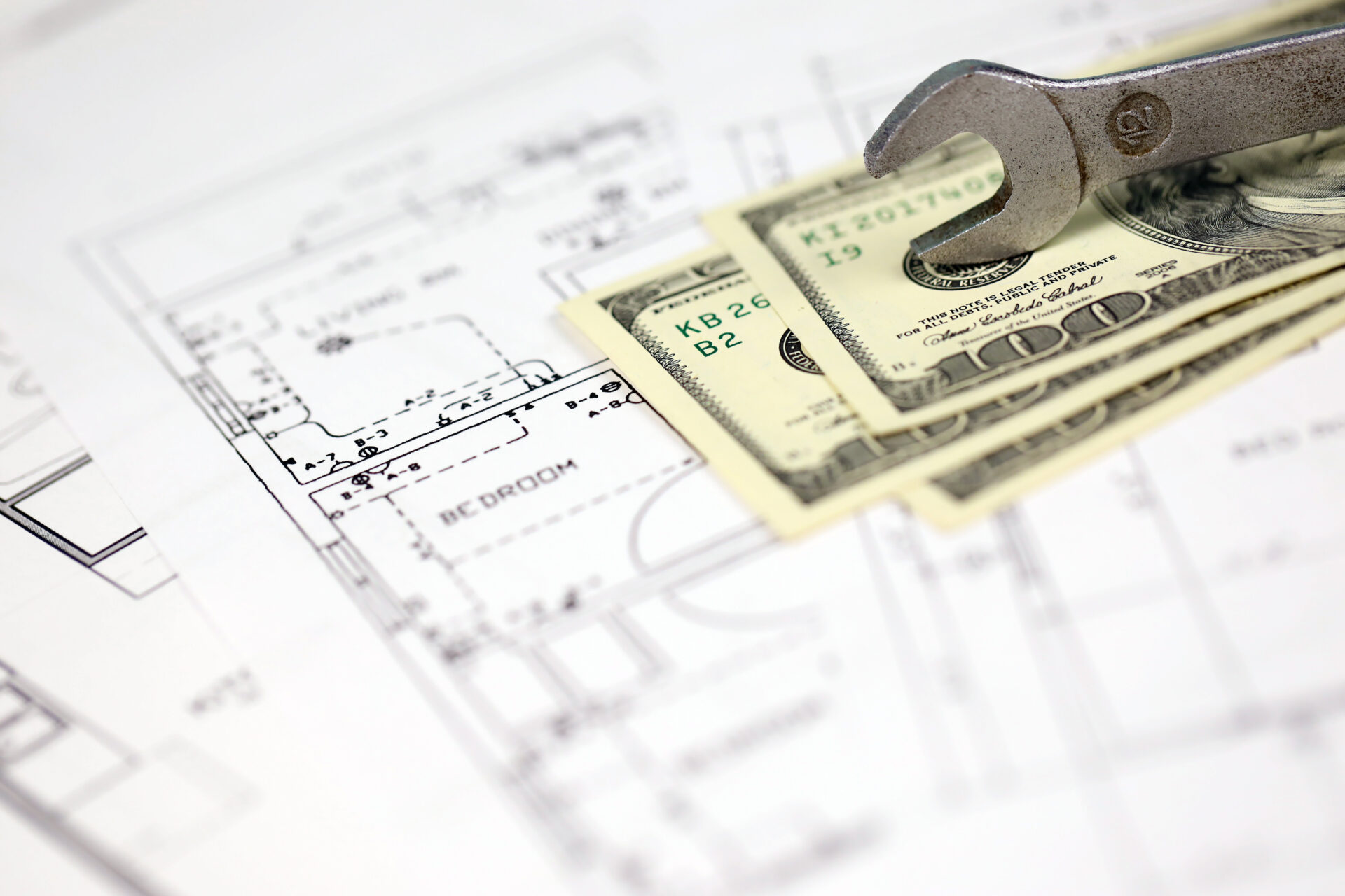 spanner on top of money with blueprints of residential house plan. restoring, repair, service maintenance cost