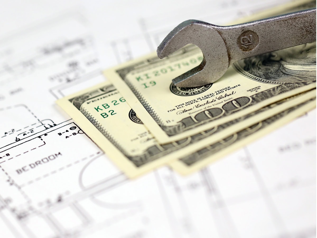 spanner on top of money with blueprints of residential house plan. restoring, repair, service maintenance cost