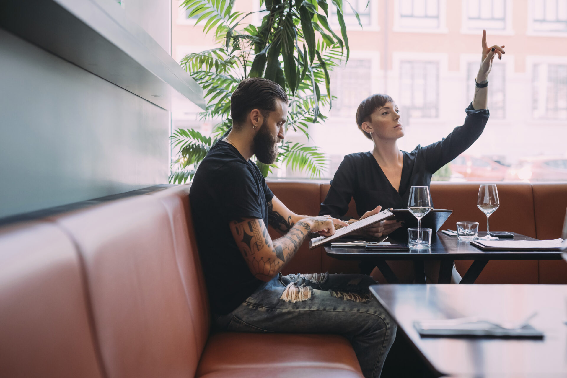 young couple sitting at a table in a bar, woman beckoning for the bill.